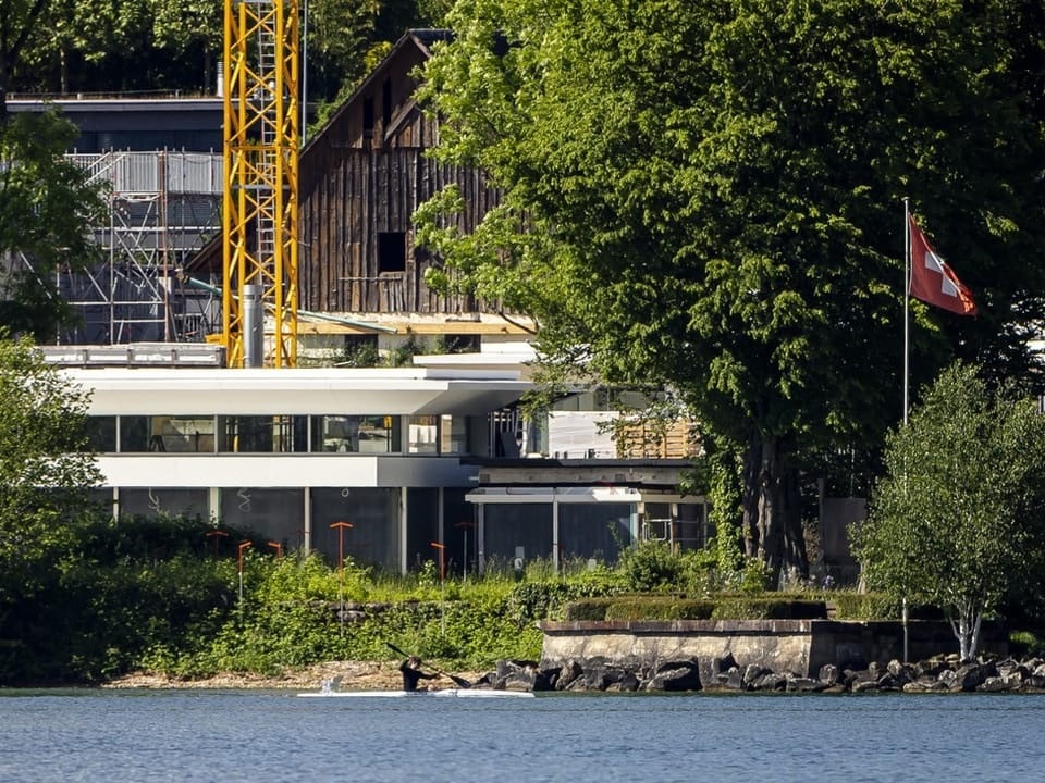 Moderne Gebäude am See mit Schweizer Flagge im Vordergrund.