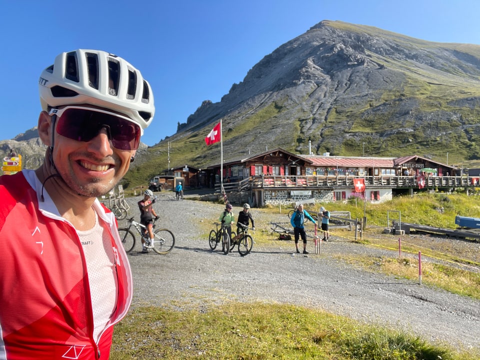 Mountainbiker Andreas Wieland vor Berghütte mit Schweizer Flagge.