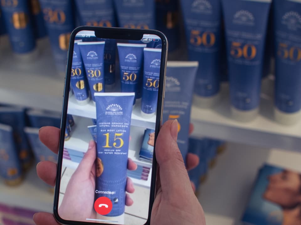 Eine Hand hält ein Smartphone, das eine Flasche Sonnenlotion in einem Geschäft zeigt.