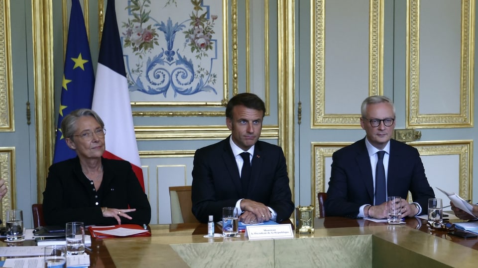 Borne, Macron und Le Maire sitzen in einer Reihe während einer Medienkonferenz.