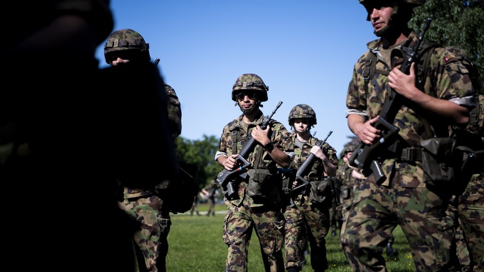 Soldaten in Tarnkleidung mit Gewehren beim Marschieren auf einer Wiese.