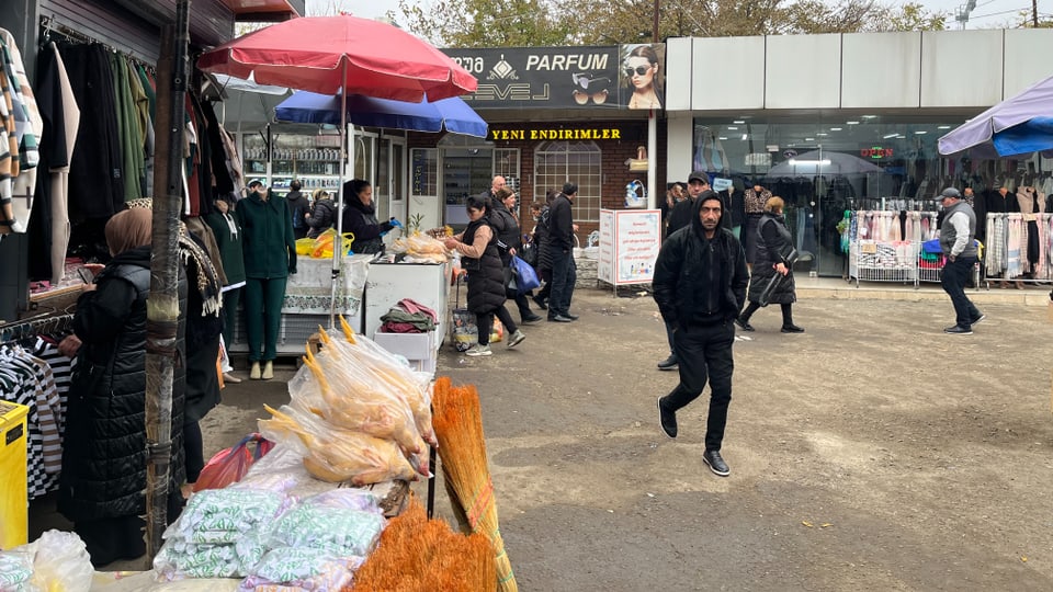 Markt mit Ständen und Passanten bei Bekleidungsgeschäft.