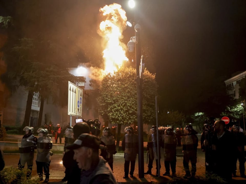 Polizisten bei Nacht vor einem brennenden Baum.