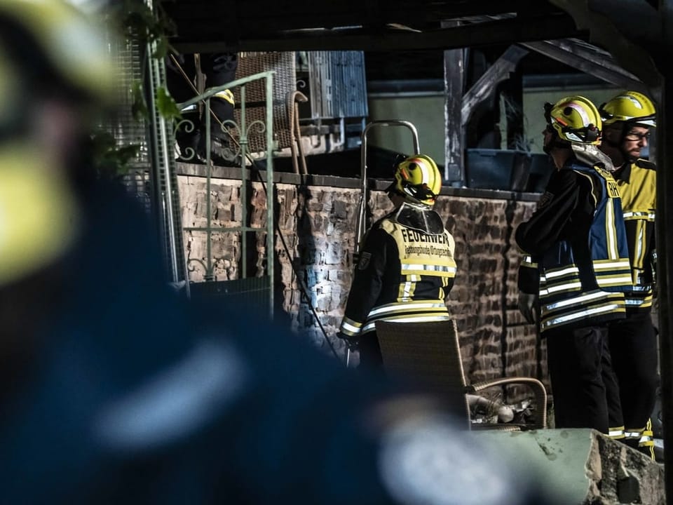 Feuerwehrleute in gelben Helmen bei einem Einsatz vor einer gemauerten Wand.