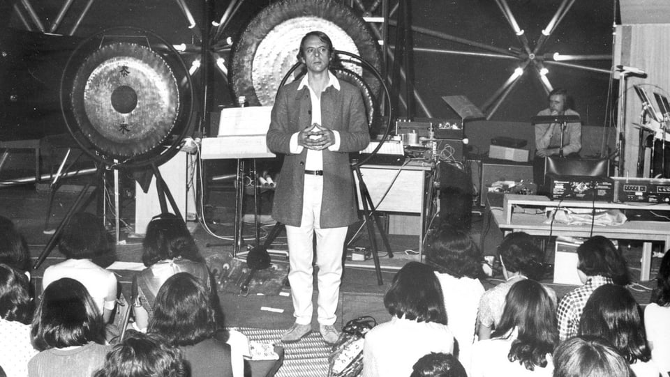 Stockhausen vor grossen Gongs auf einer Bühne vor jungem Publikum