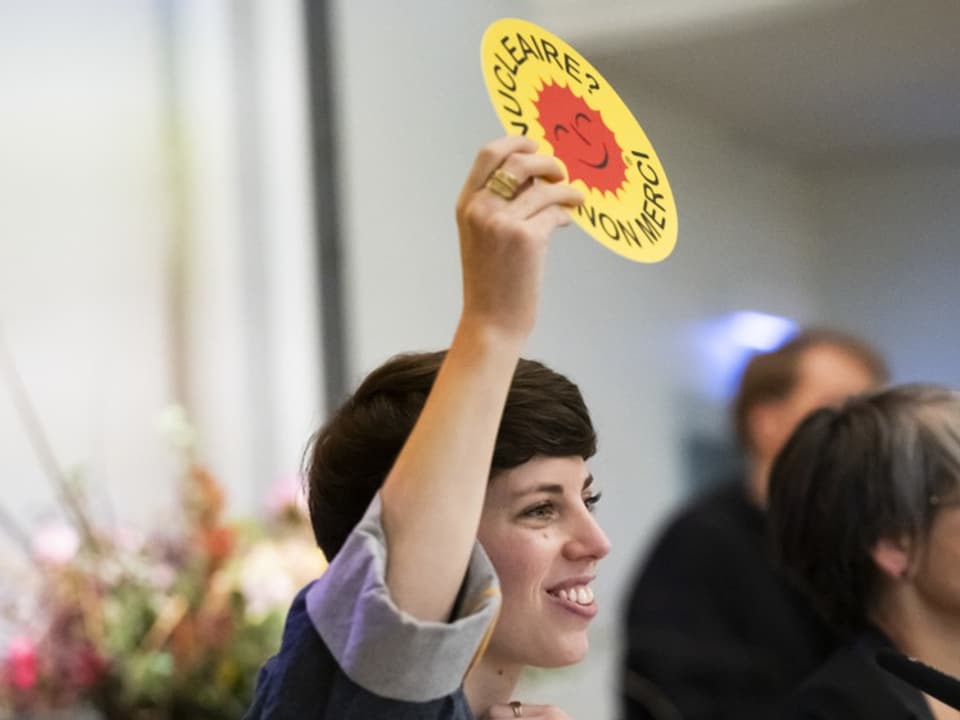 Frau hält gelbes Schild mit Aufschrift 'Nucléaire? Non Merci'.