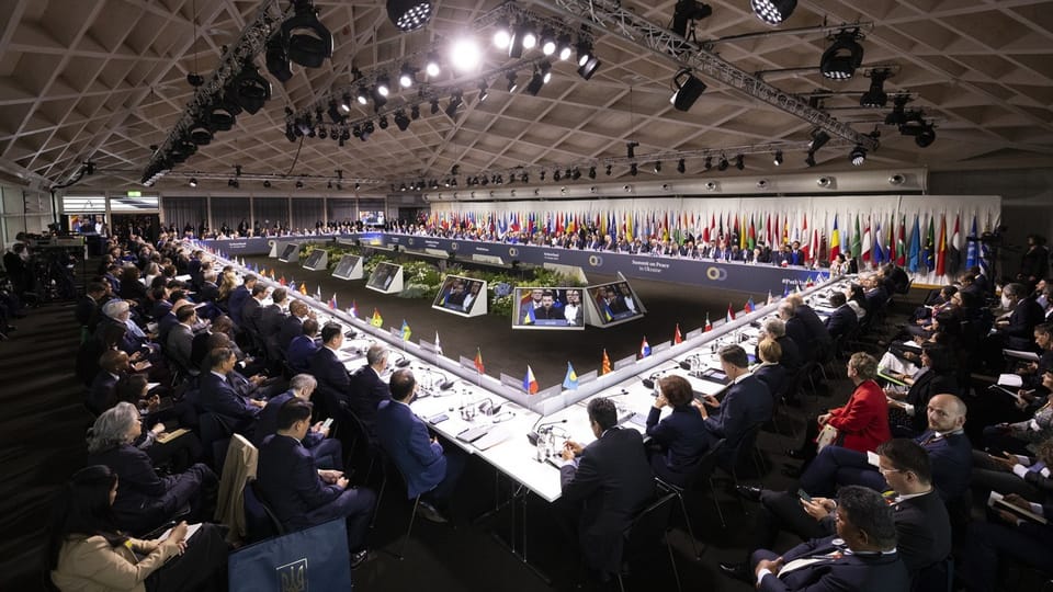 Teilnehmer sitzen an einem grossen Konferenztisch in einem Konferenzsaal.