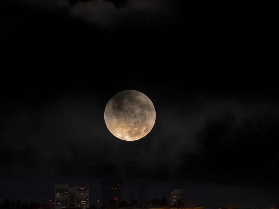 Vollmond am Nachthimmel über einer Stadt.