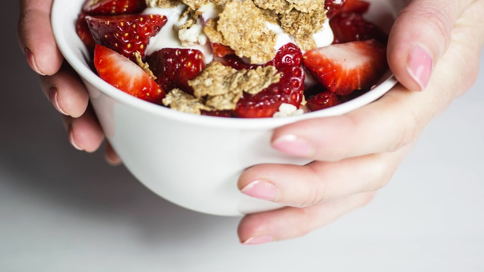 Eine Schale Müsli mit Beeren, gehalten von zwei Händen.