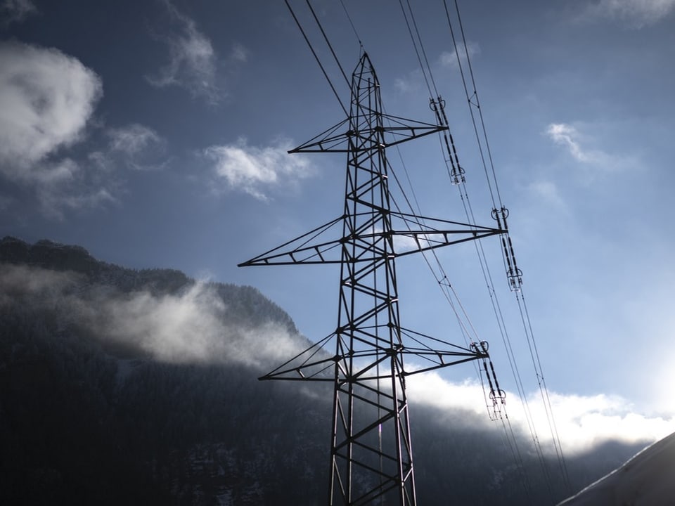 Strommast vor bewölktem Himmel und Bergen.