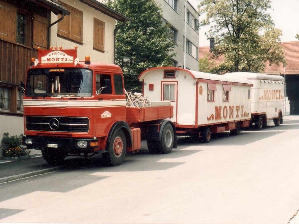 Roter Lastwagen von Zirkus Monti mit Wohnwagen auf einer Strasse.