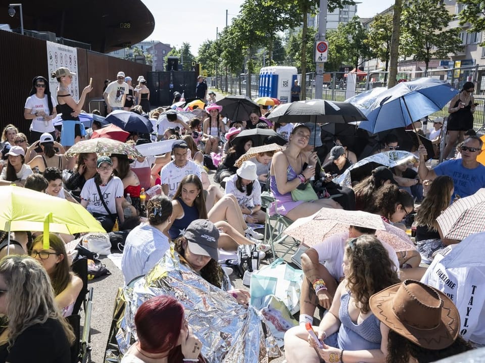 Menschenmenge mit Sonnenschirmen sitzt im Freien.