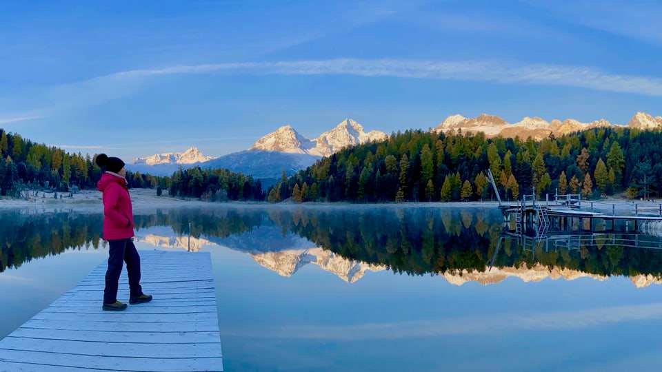 Person auf dem Steg am See mit Bergblick.