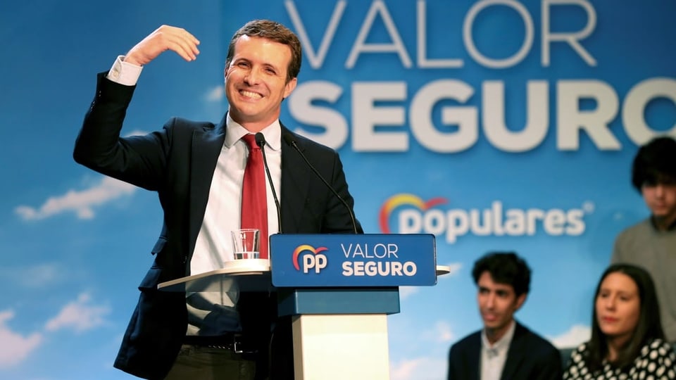 Pablo Casado spricht an einer Wahlkampfverantsaltung. Er trägt einen schwarzen Blazer, rote Krawatte und hebt die rechte Hand.