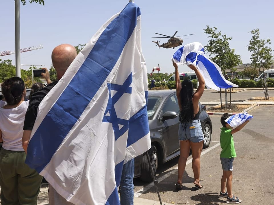 Menschen halten israelische Flaggen und jubeln einem vorbeifliegenden Hubschrauber zu.