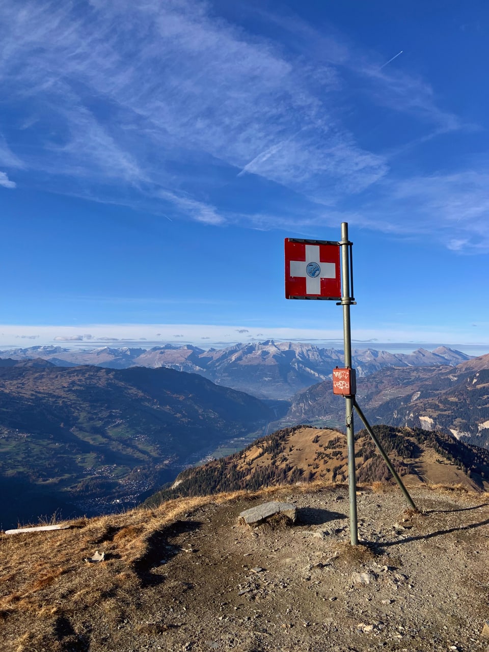 Bergpanorama mit rot-weissem Schild auf Gipfel.