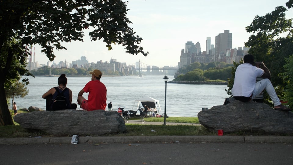 Menschen sitzen auf Felsen, im Hintergrund East River und Manhattan.
