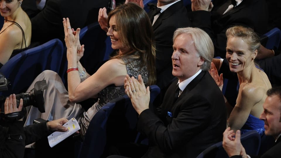 James Cameron sitzt im Rahmen der Oscarverleihung 2010 hinter seiner Exfrau Kathryn Bigelow. Beide klatschen gutgelaunt.