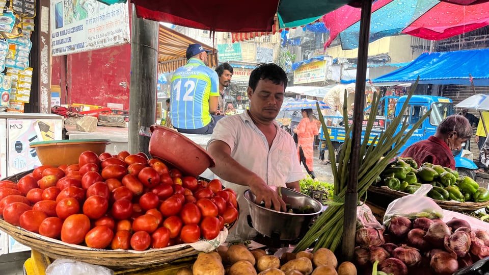 Ein Mann steht hinter einem Marktstand, im Vordergrund ein Korb mit Tomaten
