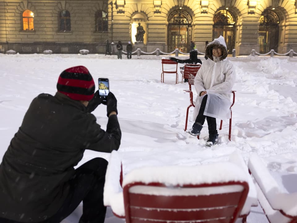 Person sitzt im Schnee auf einem Stuhl, jemand macht ein Foto.