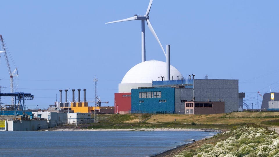 Kernkraftwerk und Windkraftanlage an einem Flussufer.