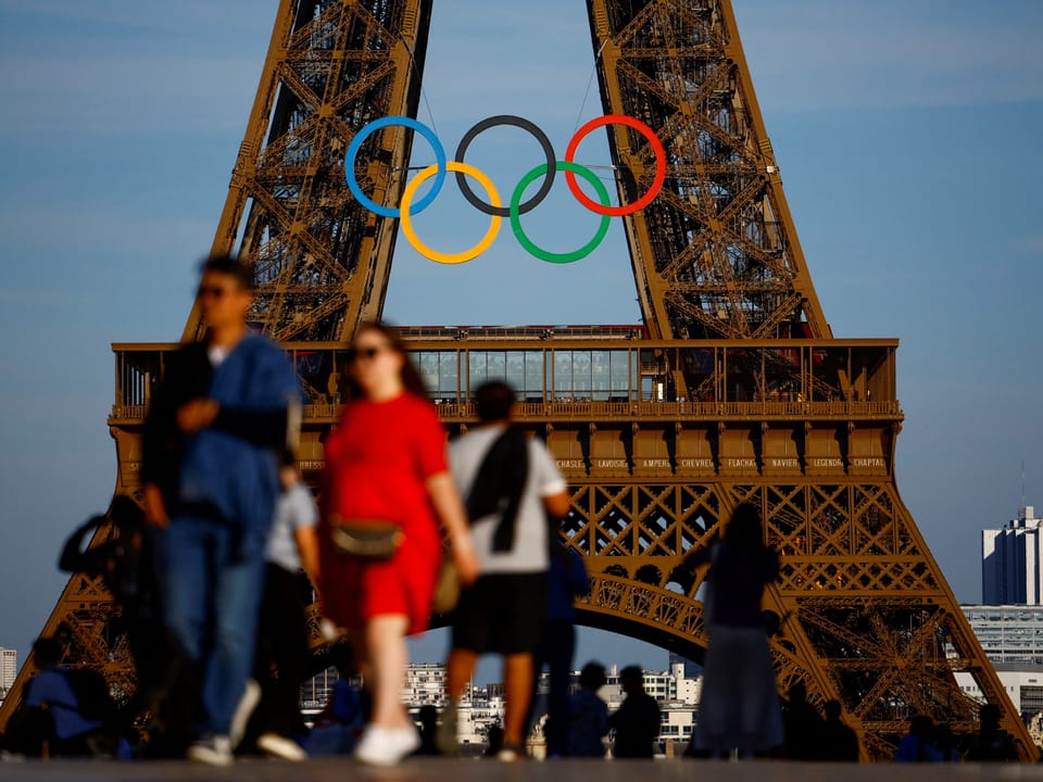 Menschen gehen vor dem Eiffelturm mit Olympischen Ringen.