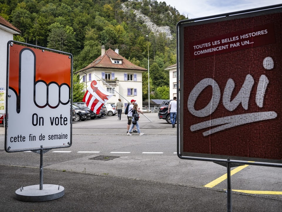 Zwei Plakate zur Abstimmung, Strasse und Gebäude im Hintergrund.