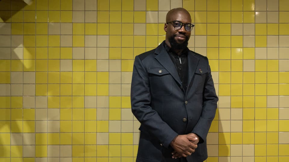 Stephen Manzini in einem schwarzen Anzug vor einer gelben Wand im Soweto-Theater. 