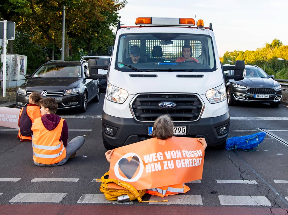 Protestierende sitzen vor einem Lieferwagen auf der Strasse.