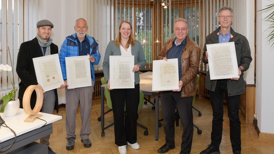 Fünf Personen halten gerahmte Dokumente in einem Büro.