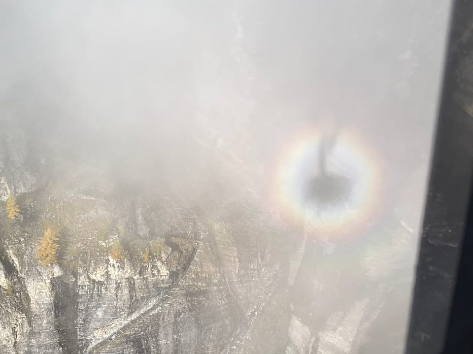 Regenbogenkreis in nebliger Berglandschaft.