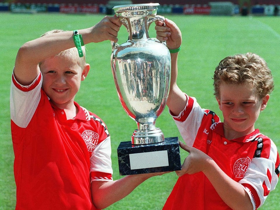 Zwei Kinder in roten Trikots halten einen grossen Pokal hoch.