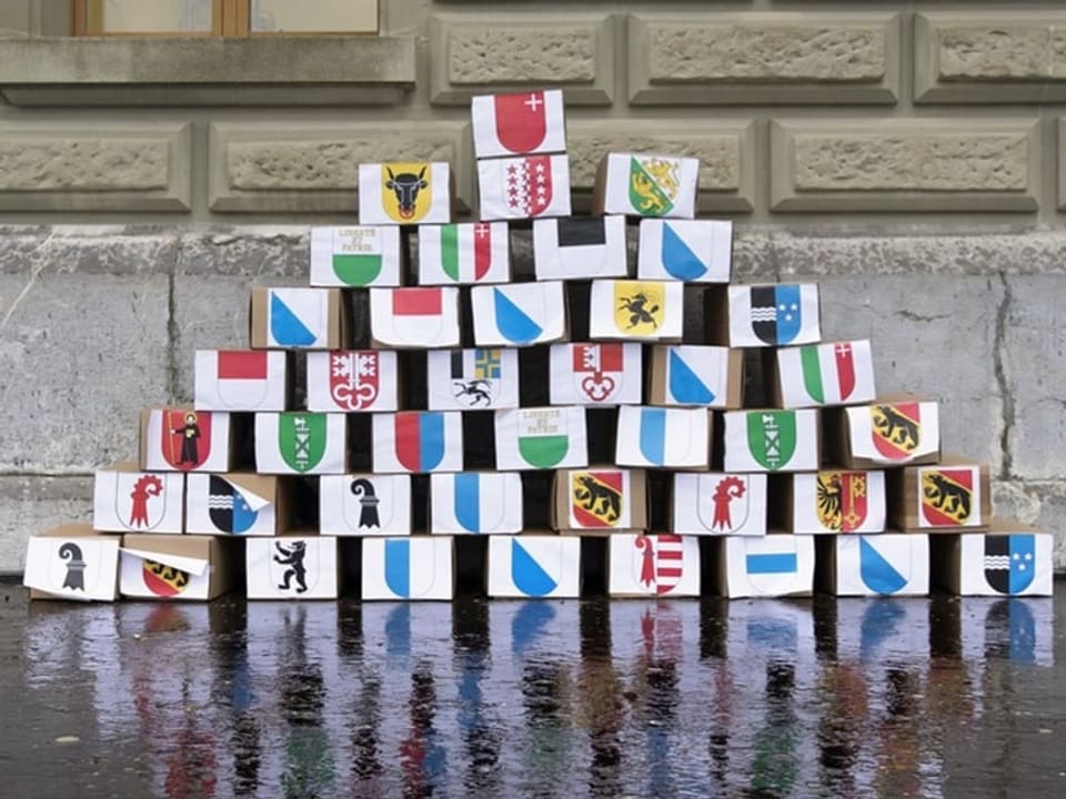 Bauklötze mit Wappen in Pyramidenform vor einer Wand.