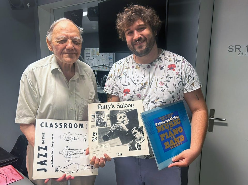 Ein alter Mann und eine junge Person mit Locken, beide halten Schallplatten in den Händen und schauen in die Kamera.