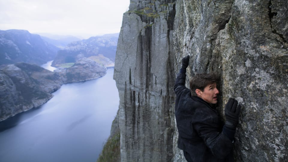 Tom Cruise hält sich an den Felsen einer Klippe fest.