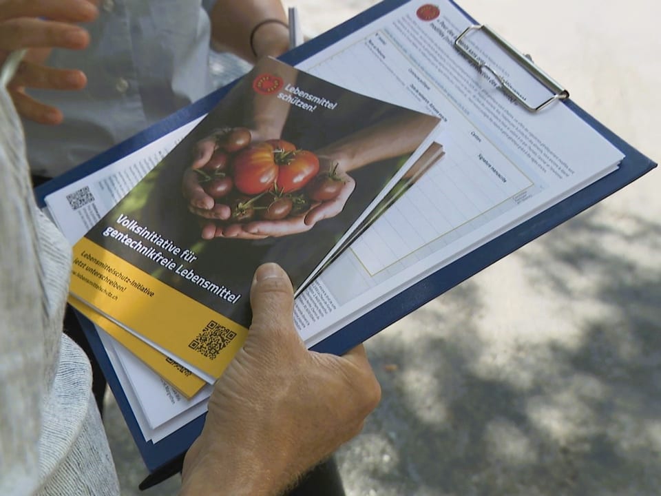 Person hält einen Klemmbrett mit einem Flyer für gentechnikfreie Lebensmittel.