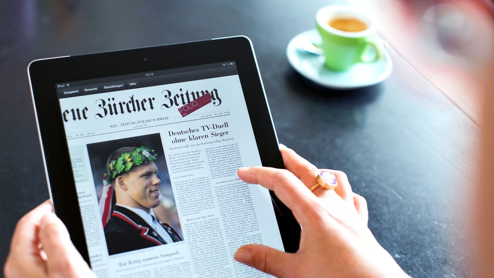 Eine Frau hält ein Tablet in der Hand, darauf eine Seite der «NZZ».