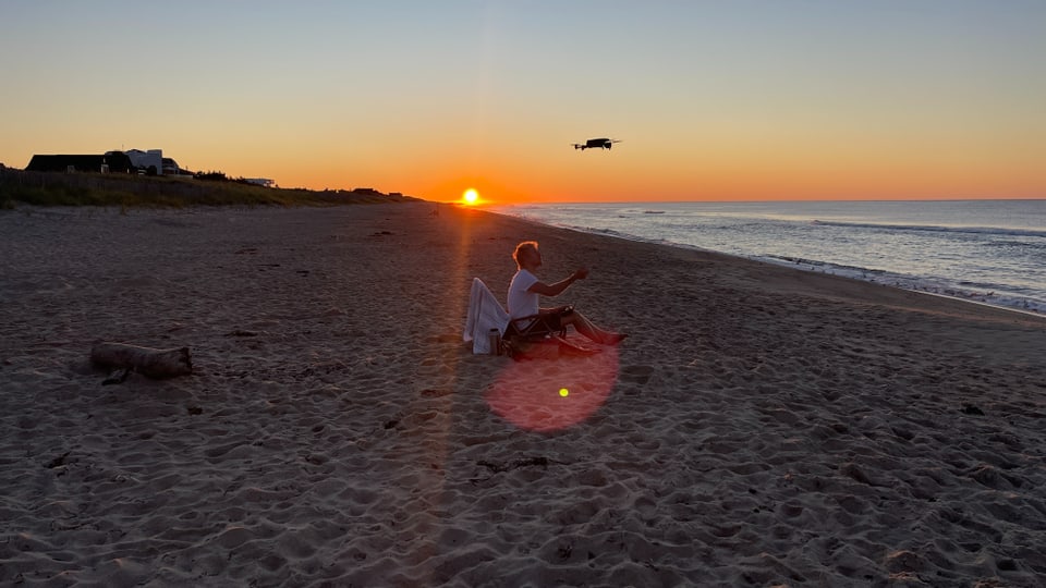 Strand mit Sonnenaufgang, ein junger Mann schickt seine Drone los