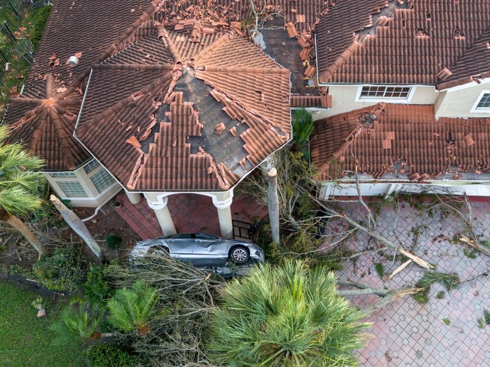 Auto auf Dach, beschädigtes Haus durch Sturm.