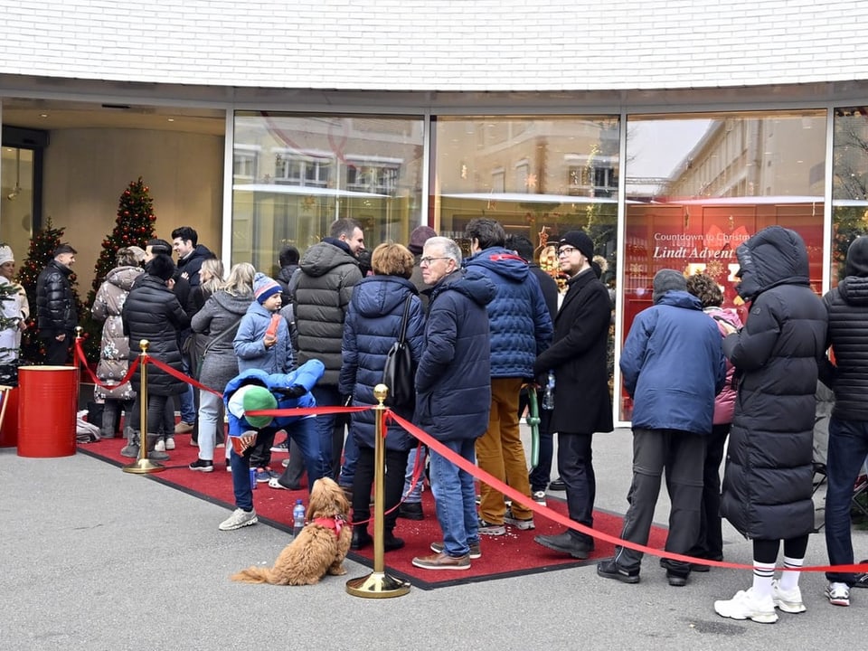 Menschen in Winterkleidung stehen Schlange vor einem Ladengeschäft.