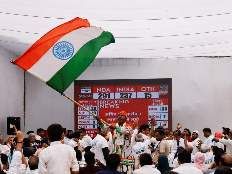 Menschen jubeln mit indischer Nationalflagge vor einem grossen Bildschirm.