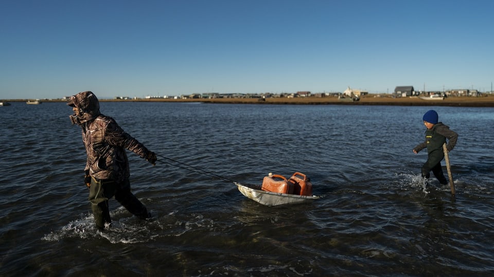 Zwei Menschen ziehen einen Schlitten mit Treibstoffbehältern durch die Lagune zu ihrem Boot. 