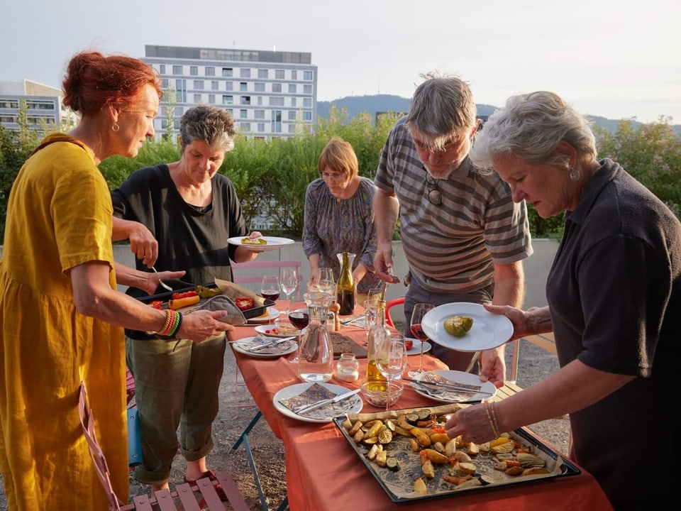 Fünf Personen essen gemeinsam im Freien an einem Tisch.