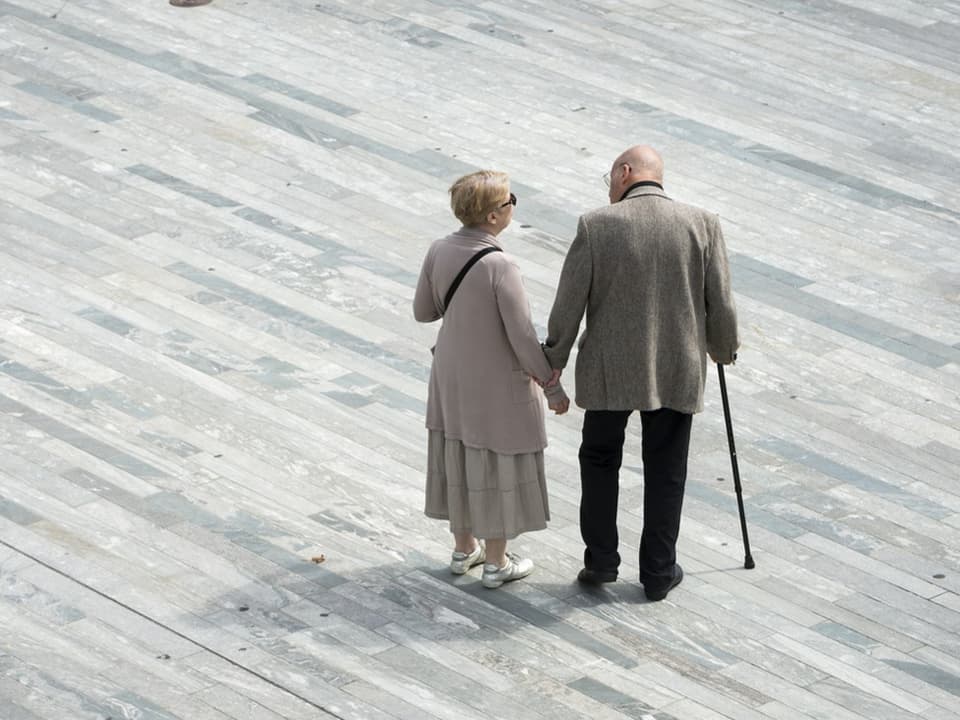 Älteres Paar spaziert Hand in Hand auf einem steinigen Gehweg.