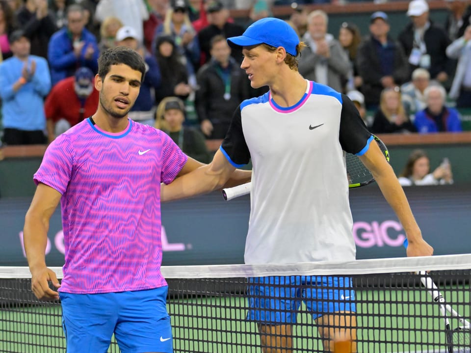 Zwei Tennisspieler reichen sich die Hand am Netz nach einem Match.