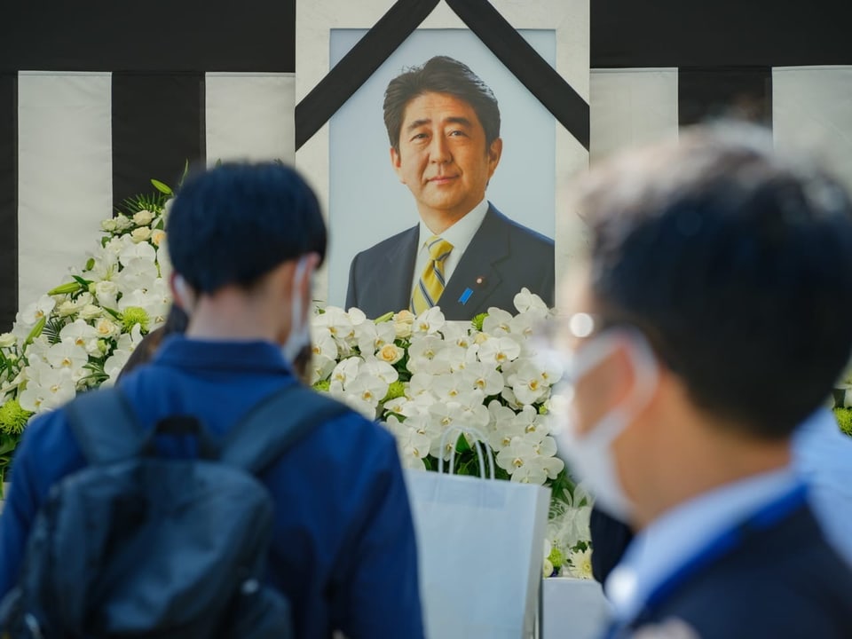 Menschen legen vor einem Bild von Shinzo Abe Blumen nieder.