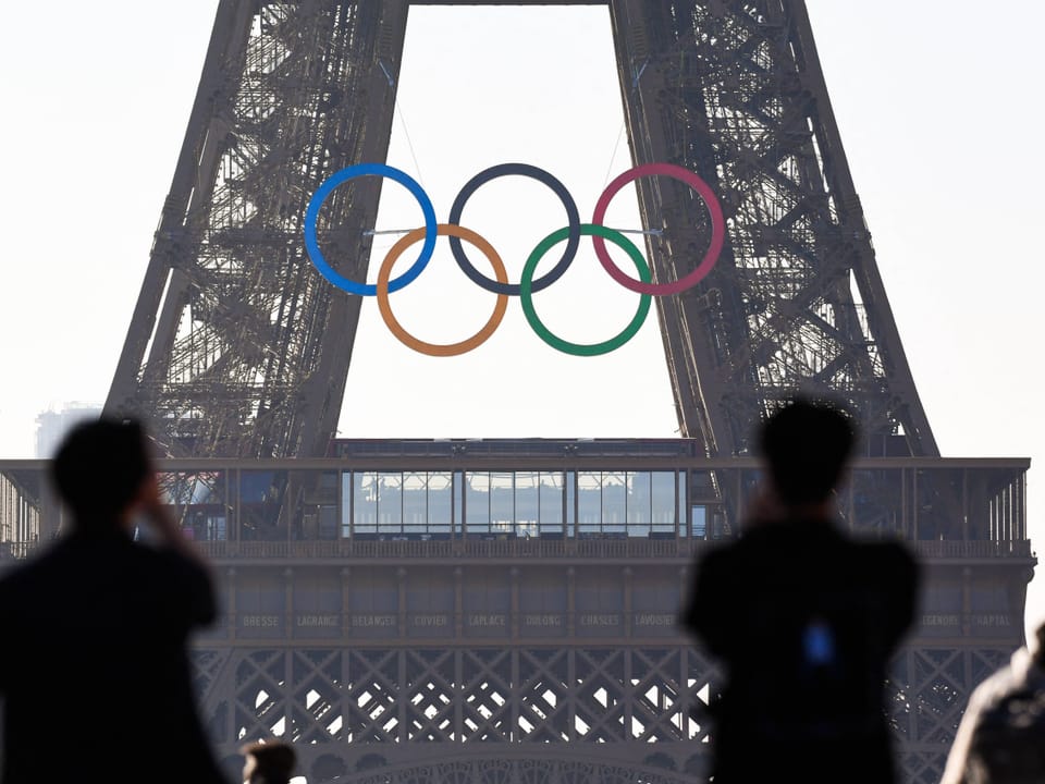 Zwei Personen betrachten olympische Ringe am Eiffelturm.