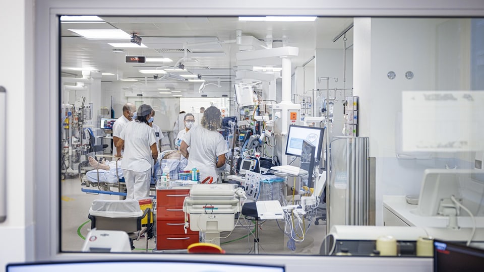 Blick in ein Spital. Mehrere Angestellte stehen um einen Patienten im Krankenbett.