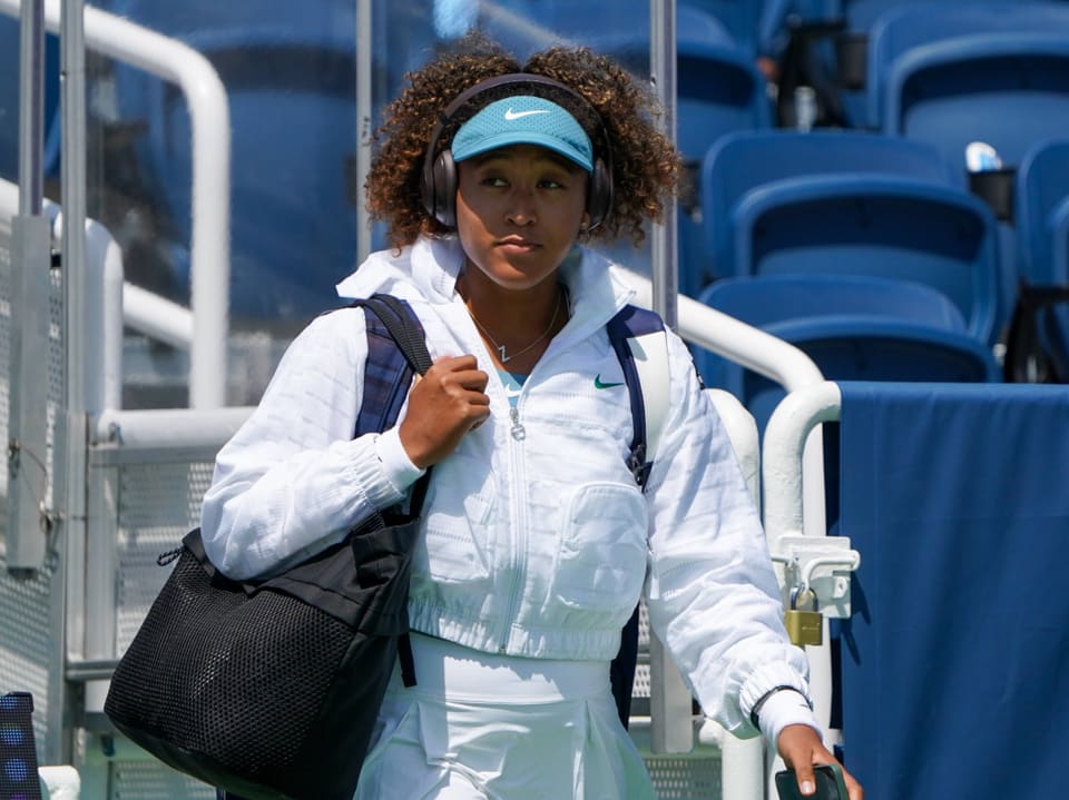 Tennisspielerin in weissem Outfit und Kopfhörern auf dem Tennisplatz.