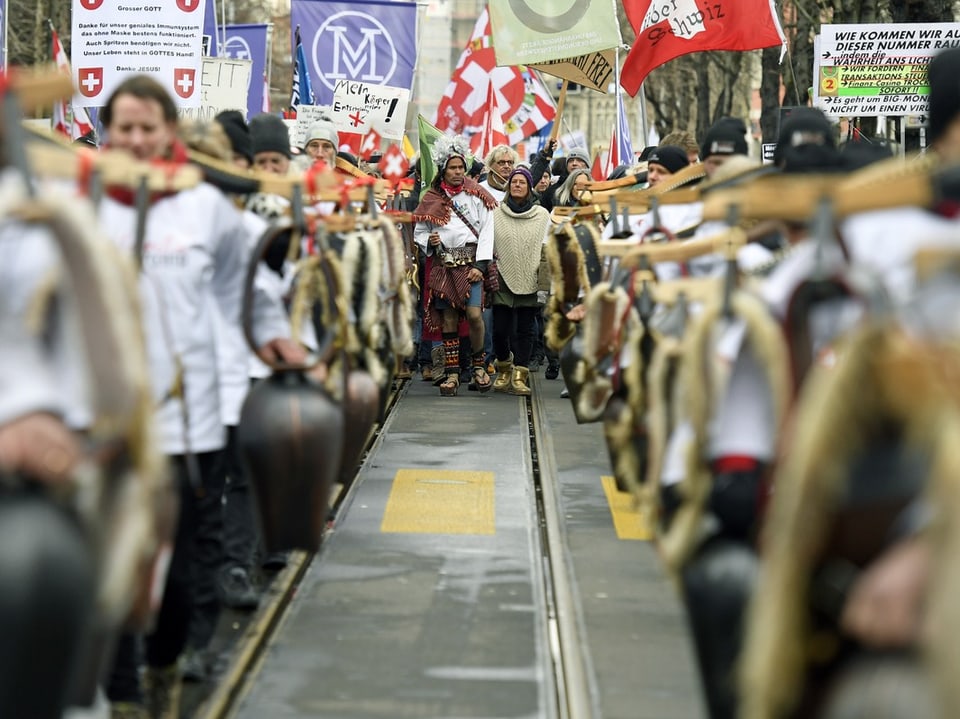 Menschen marschieren in einer Parade mit Kuhglocken und Fahnen.